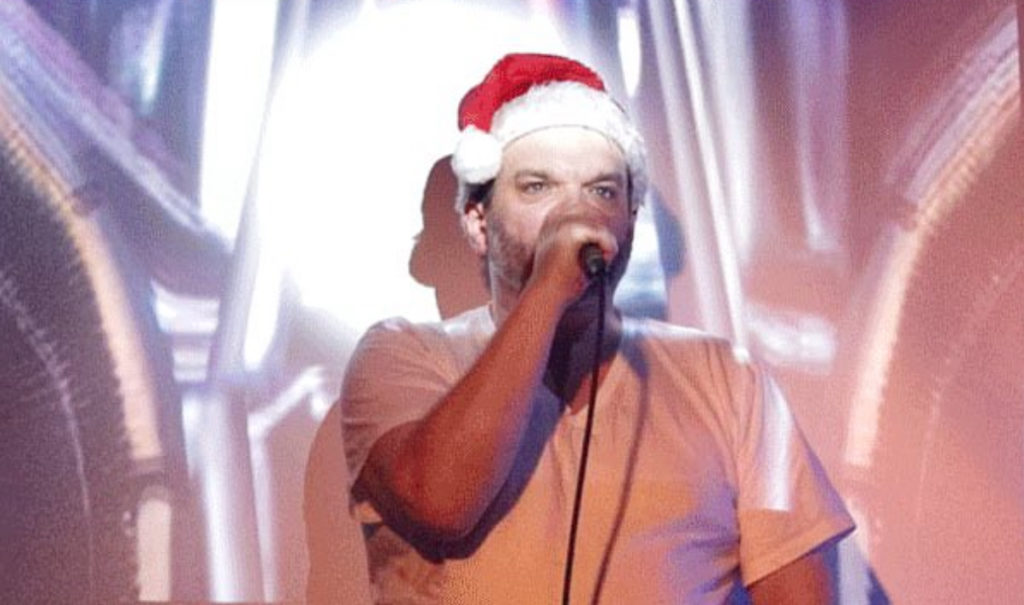 John Raymond Barker performing in a Santa hat against a projection of a space ship